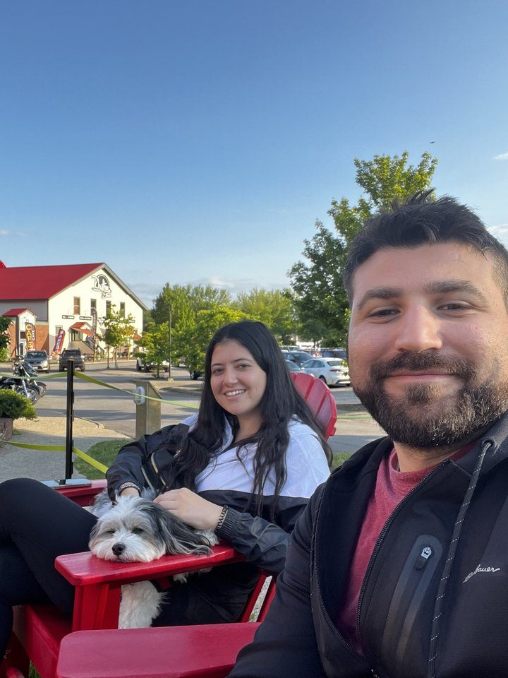 Jessica and Rami on red Adirondack chairs with a little dog curled up on Jessica's lap