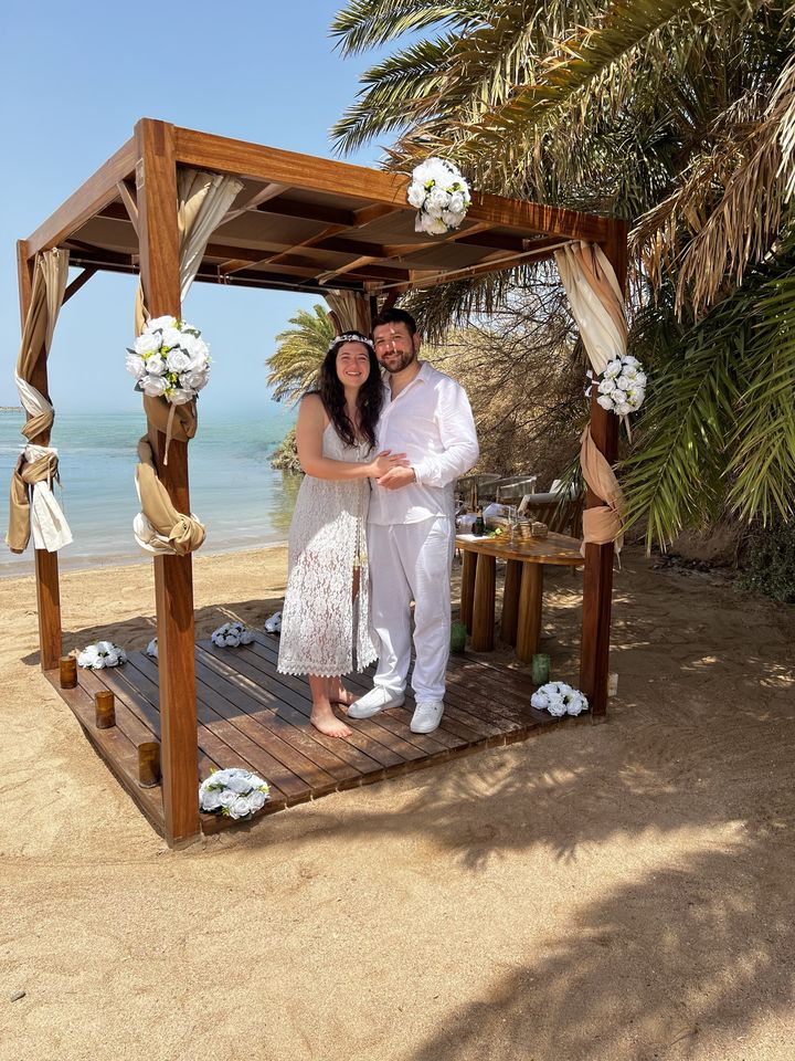 Jessica and Rami dressed in white under a beach gazebo