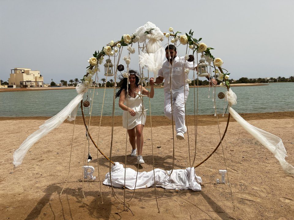 Jessica and Rami running hand in hand through a round floral arch on a lagoon beach