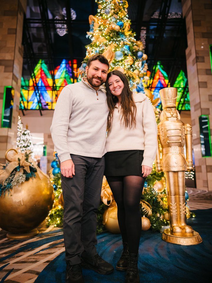 Jessica and Rami in front of a gold-and-blue Christmas tree beside a golden nutcracker