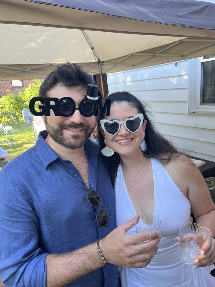Rami in GROOM glasses and Jessica in heart sunglasses, toasting at a summer party
